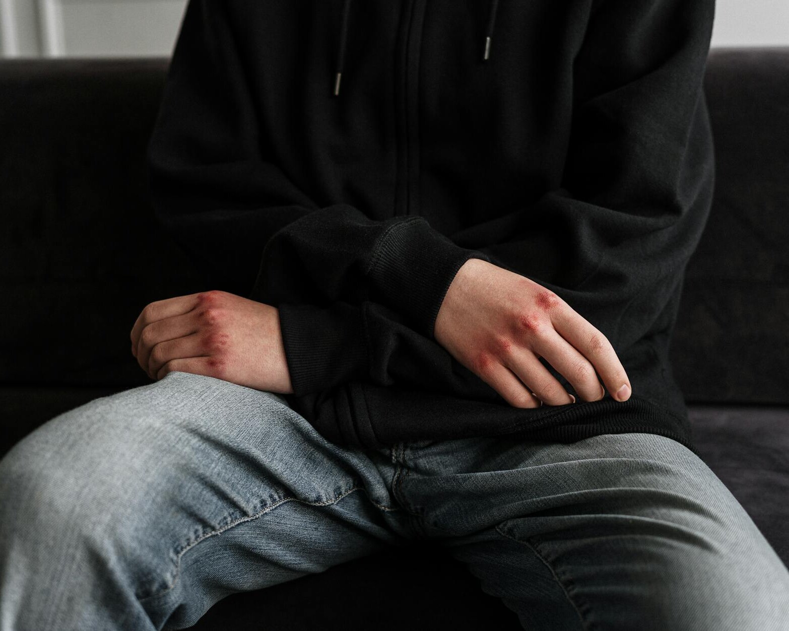 person in black jacket and blue denim jeans sitting on black couch