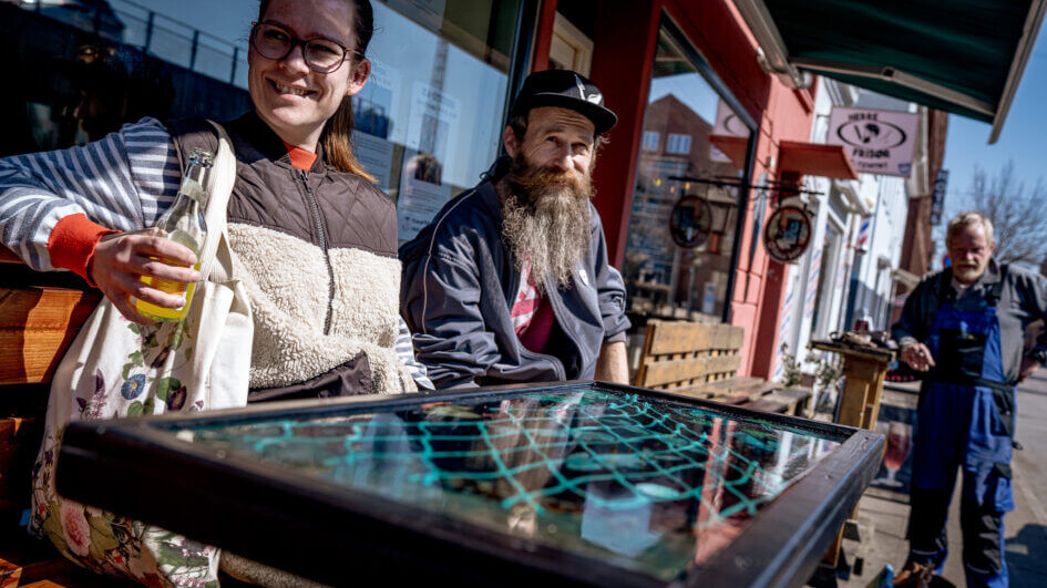 Denise Michael og Morten Runge, der har drevet Vinbaren siden 2016 prøvekører den nye borde-/bænkeinstallation med appelsinvand. Foto: Fjodor Pedersen.
