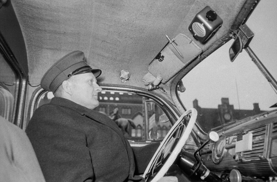 Esbjerg Taxa har indviet radioinstallationen i 17 af selskabets 28 vogne. Nu kan chaufførerne dirigeres fra taxakontoret i Strandbygade.
Bag rattet ses Holger Nielsen. Foto: Esbjerg Byhistoriske Arkiv.