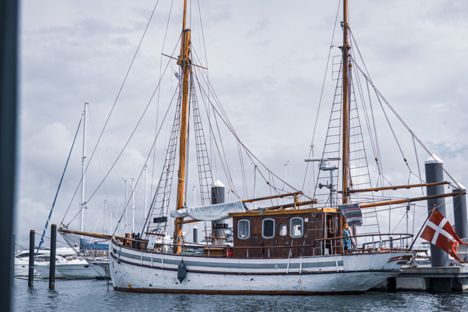 Et klassisk træskib vugger i marinaen – havnens charme får følgeskab af lyserøde cowboyhatte og grin ombord på nabobåden. Foto: Fjodor Pedersen.