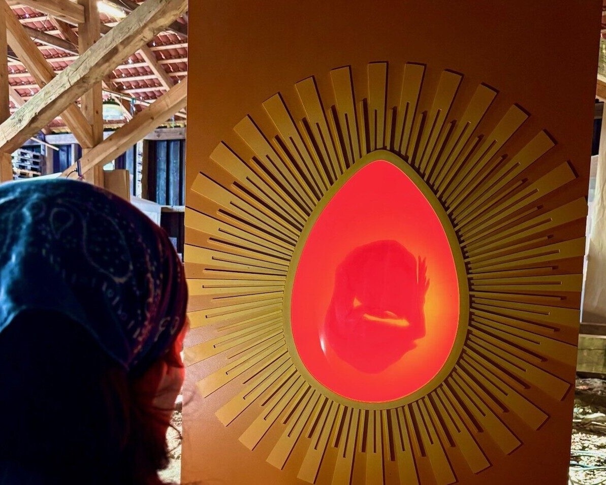 En tilskuer betragter det lysende æg, hvor Marthas skikkelse toner frem – et symbol på både liv og tab i forestillingen MARTHA! Foto fra prøverne.