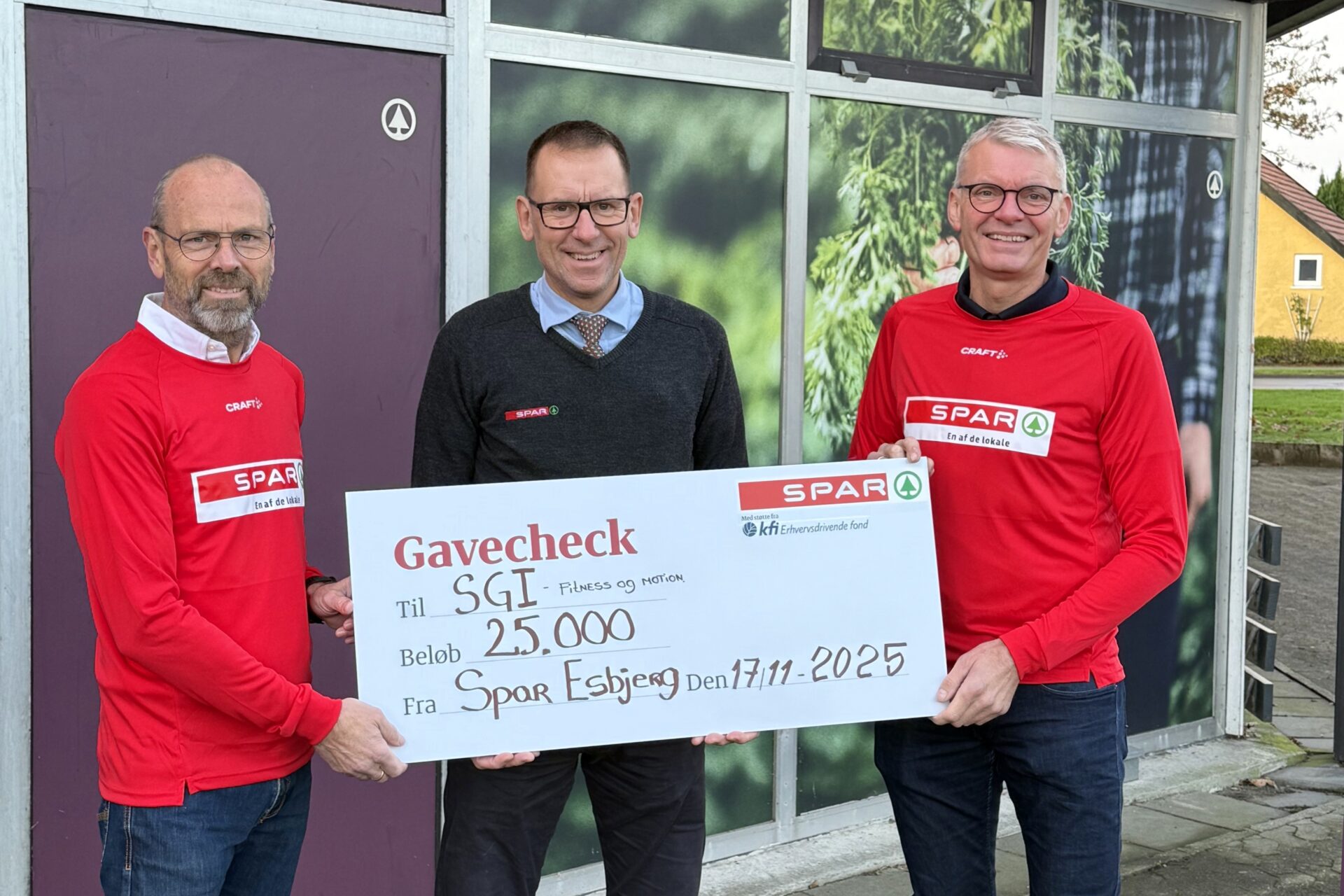SPAR-købmand Hans Boel Lauridsen overrækker en gavecheck på 25.000 kroner til SGI Fitness & Motion foran butikken i Østerbyen.