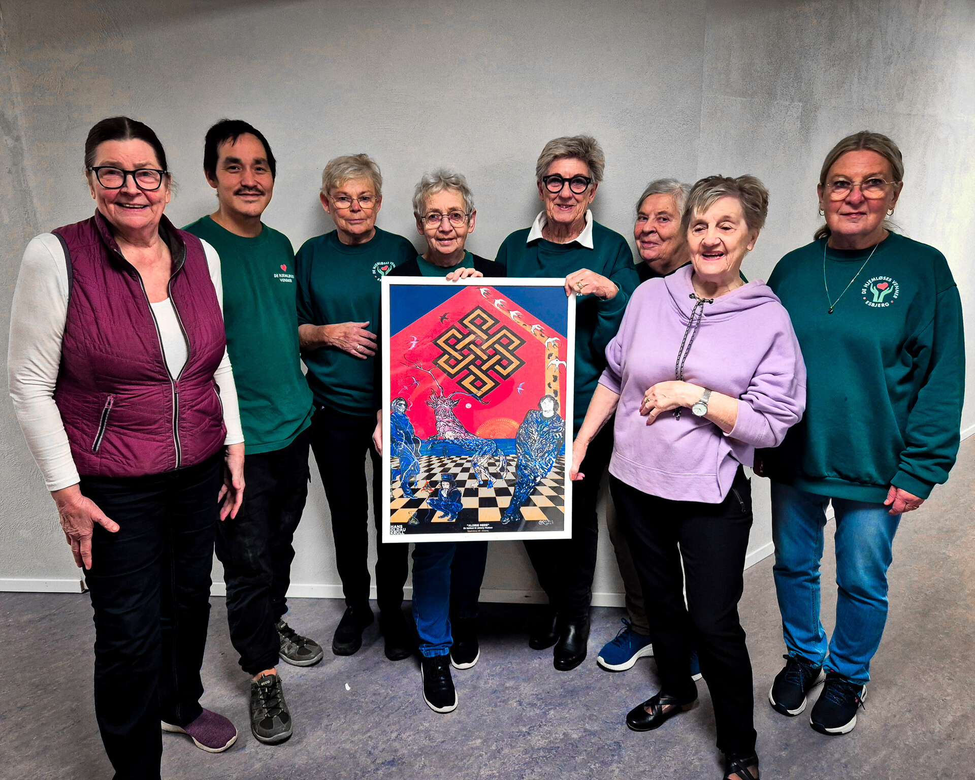 Frivillige fra De Hjemløses Venner i Esbjerg viser plakaten frem, der gengiver Hans Krulls Johnny Madsen-gavl og nu sælges til fordel for hjemløse og socialt udsatte. Foto: Camilla Uth.