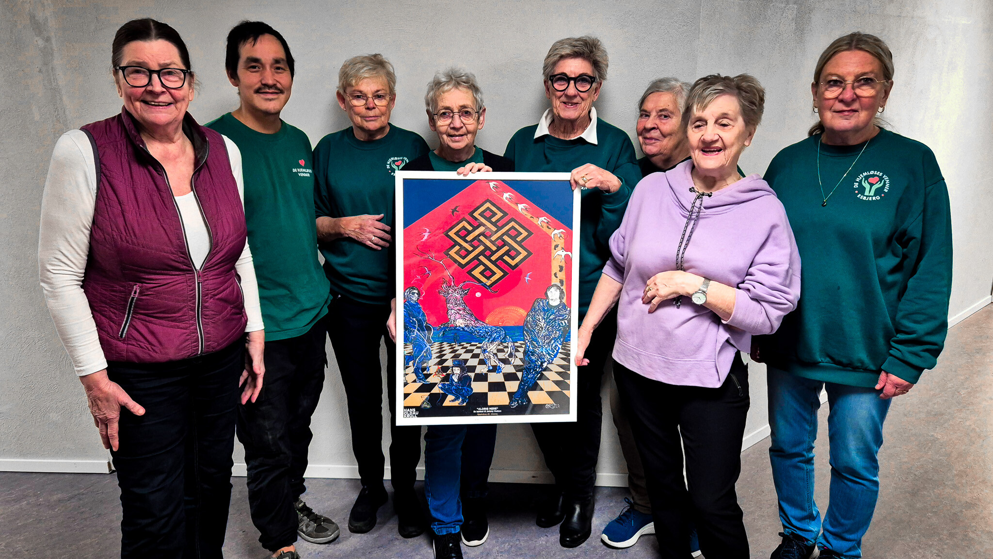 Frivillige fra De Hjemløses Venner i Esbjerg viser plakaten frem, der gengiver Hans Krulls Johnny Madsen-gavl og nu sælges til fordel for hjemløse og socialt udsatte. Foto: Camilla Uth.