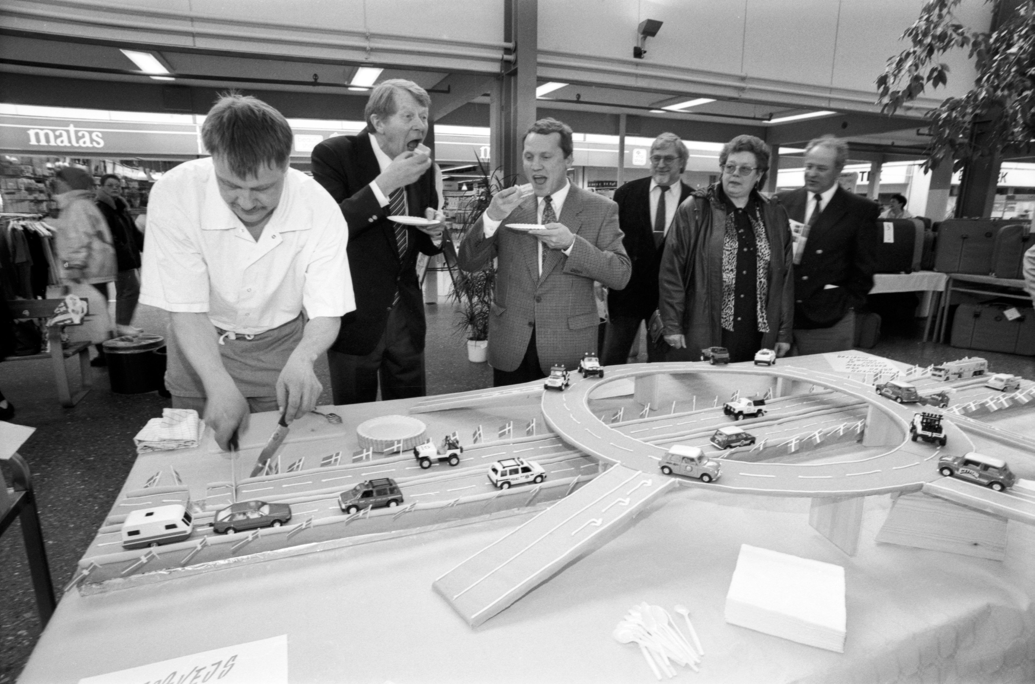 Fredag den 25. marts 1994 åbnede Vejdirektoratet en udstilling om motorvejsbyggeriet mellem Esbjerg og Kolding. Udstillingen blev vist på centertorvet i Sædding Centret. I den anledning havde Droobs konditor Henrik Sørensen fremstillet en motorvejskage, som Vejdirektør Per Milner (til venstre) og Esbjergs borgmester Johnny Søtrup spiser her for af kagen, der var lavet af fragilité, lagkagebund, nougat, smørcreme, hasselnødkrokant, solbærmarmelade, cognac og marcipan. Foto: Esbjerg Byhistoriske Arkiv.