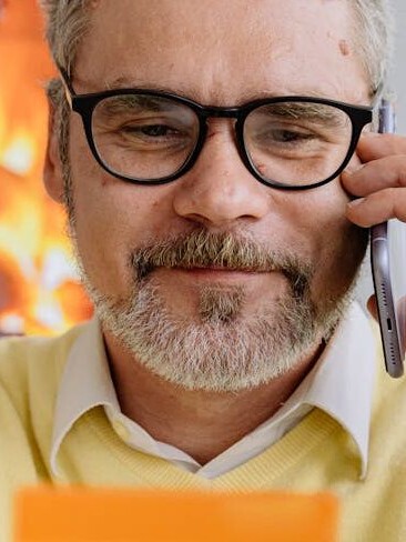 man in yelMand med kreditkort. Genrefoto: AI25.Studio Studio.low sweater wearing black framed eyeglasses holding a card while talking on phone