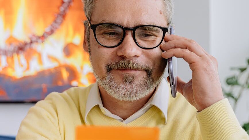 man in yelMand med kreditkort. Genrefoto: AI25.Studio Studio.low sweater wearing black framed eyeglasses holding a card while talking on phone